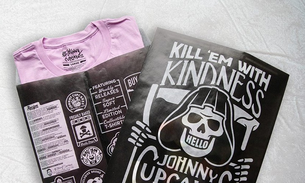 Two glassine bags with a custom package design for Johnny Cupcakes. There are two black bags printed with bold white graphics, displayed side by side with one containing a pink t-shirt.