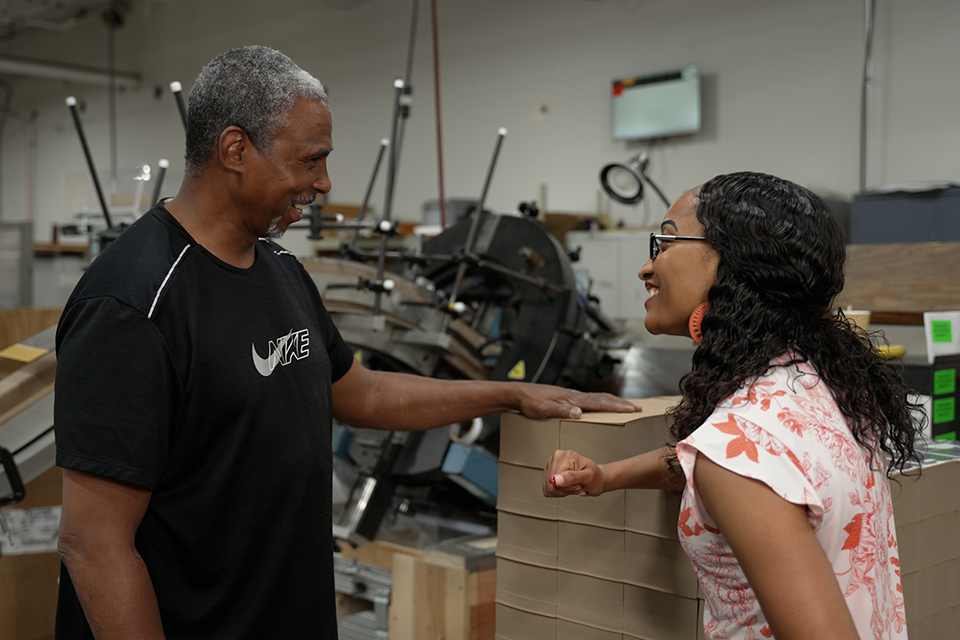 Two JBM team members laughing and talking in the packaging facility.