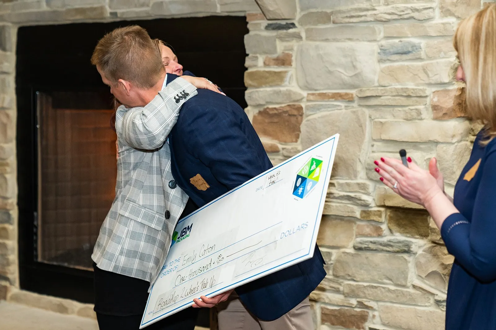 Woman hugging man holding a large check.