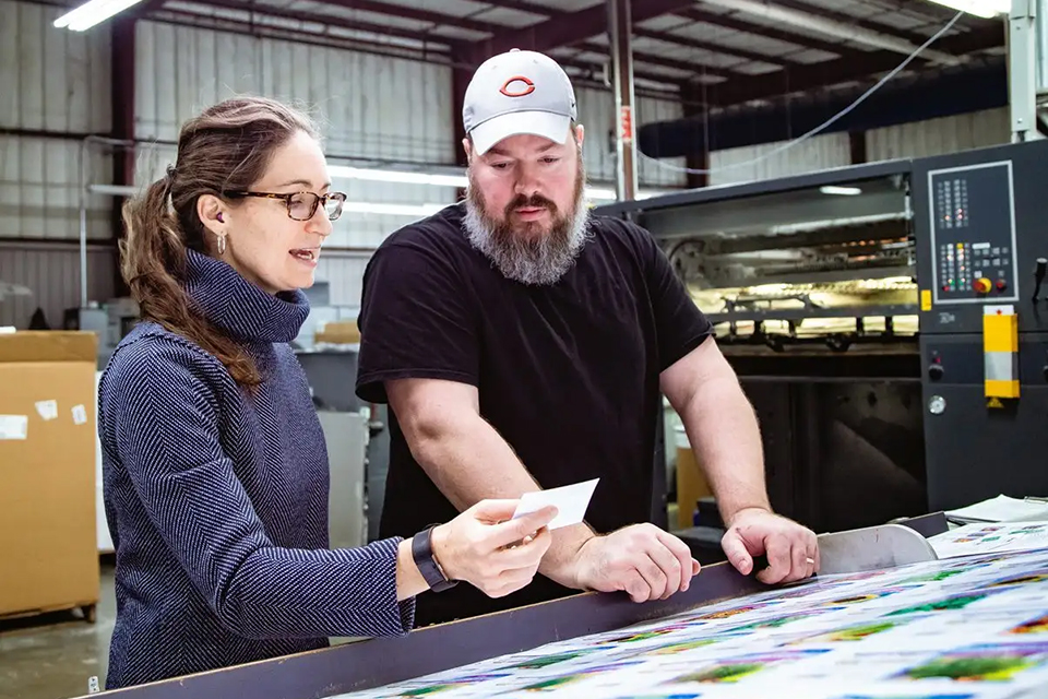 Two JBM employees working together on printing and quality checking seed packets.