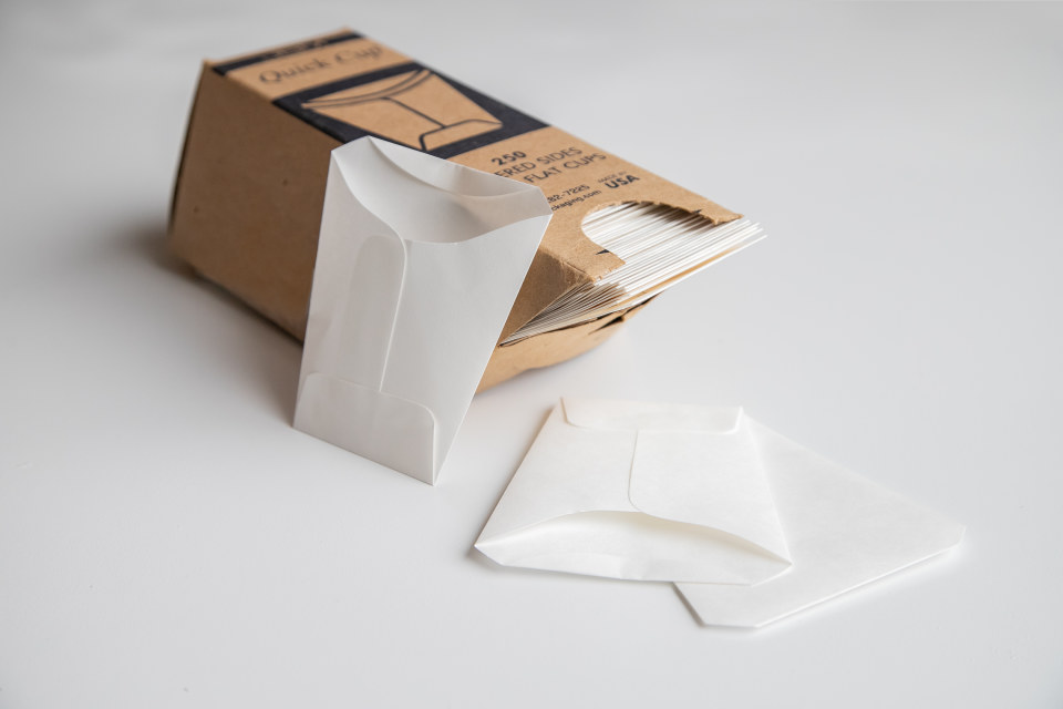 Stack of white, fold-flat disposable paper cups, showing what they look like inside and outside of the box.