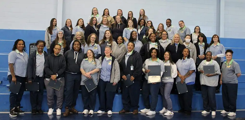 Group of incarcerated women smiling with their program graduation certificates.