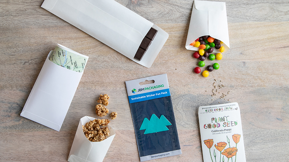 An array of different types of JBM branded packaging, including  envelopes, disposable cups, windowed packaging, and seed packaging.