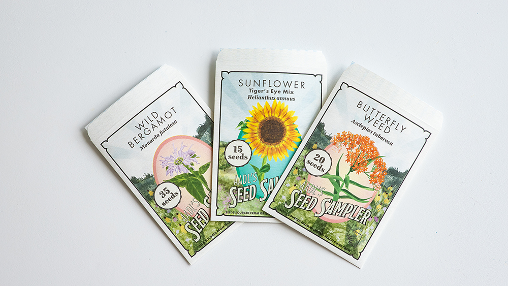 Three variety branded seed packets on a white surface with custom label text: "AADL's Seed Sampler."