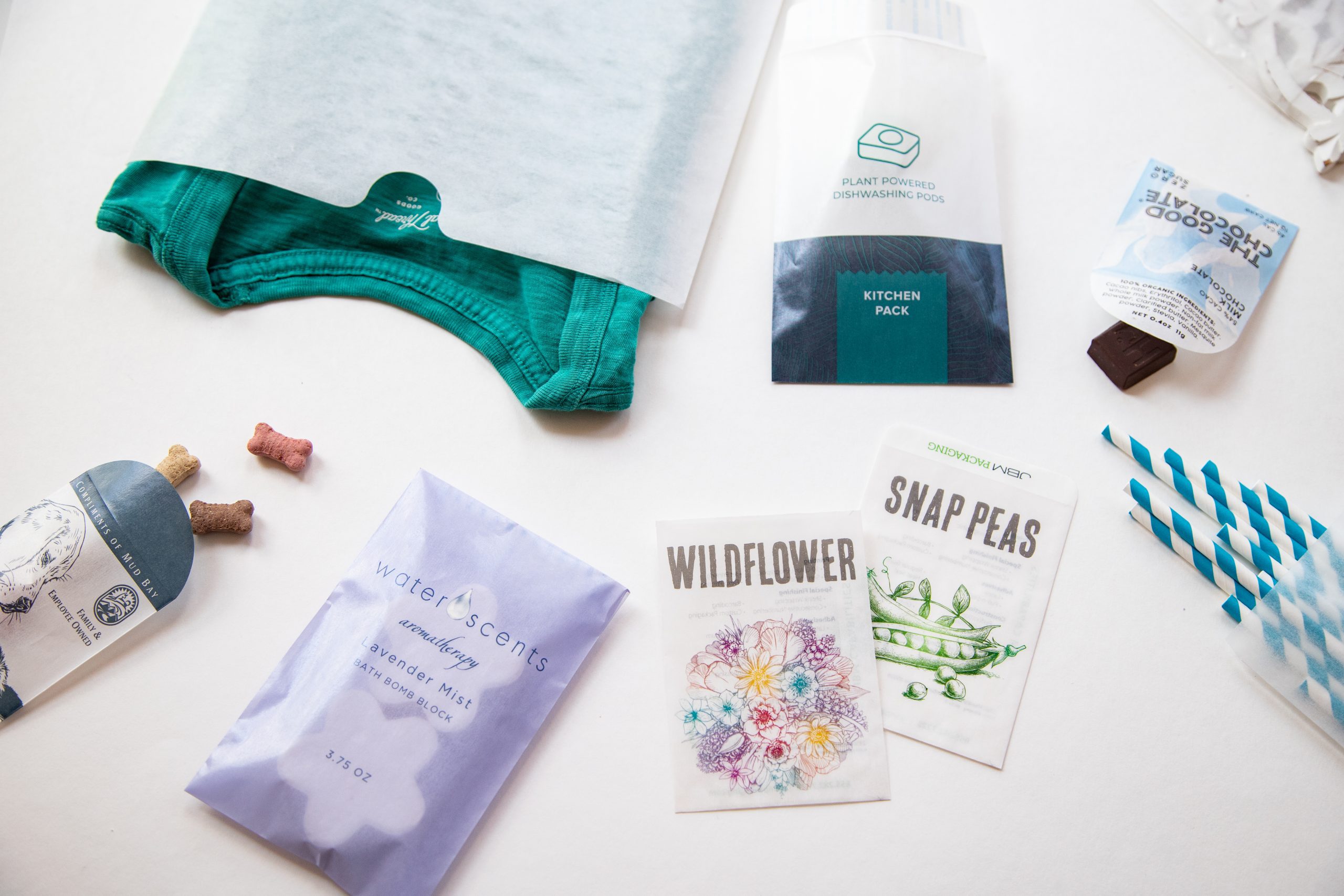 Glassine paper packages holding a variety of products: apparel, seeds, chocolate, bath products, dog treats, and straws.