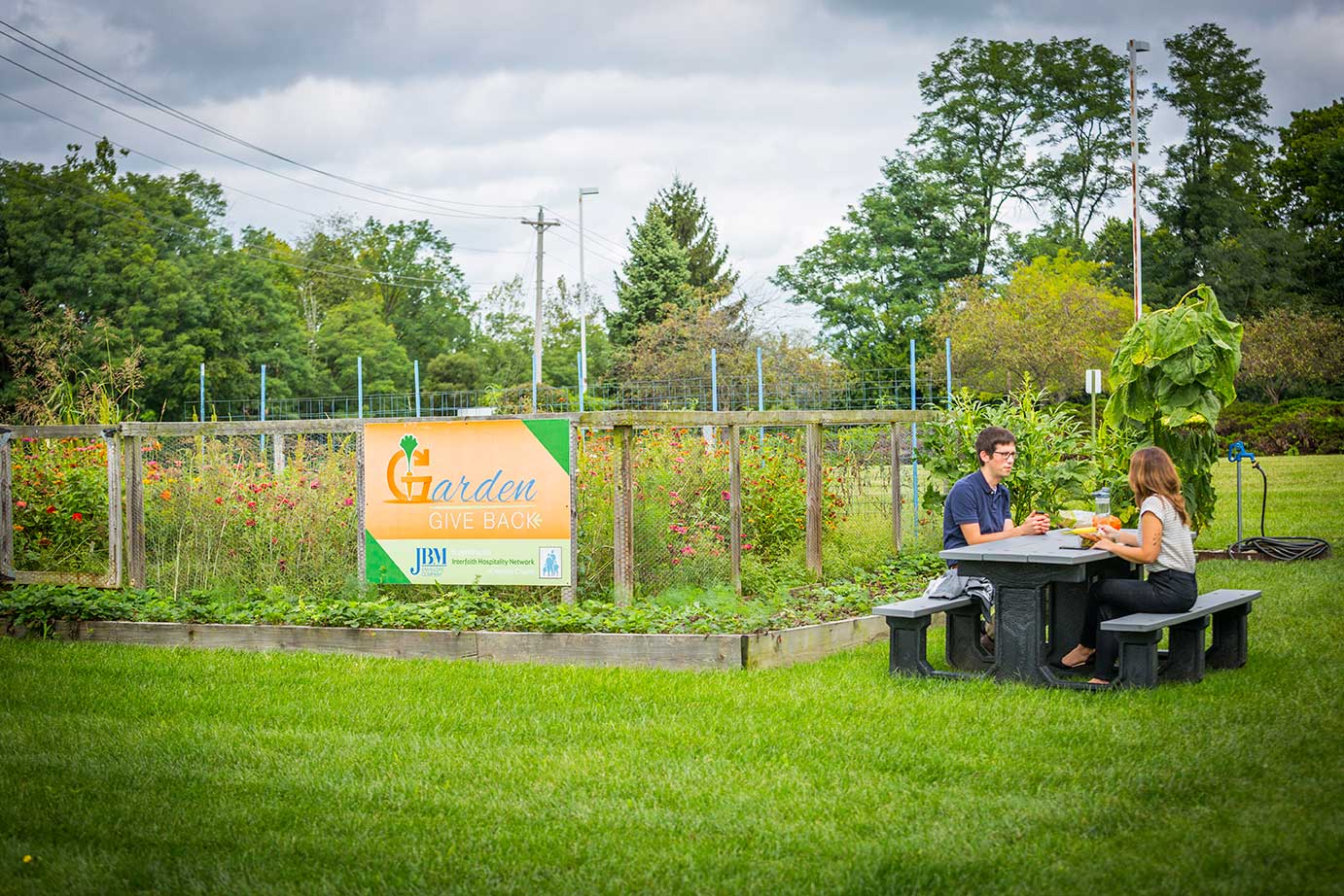The flower and vegetable garden at JBM Packaging headquarters, with two employees sitting on a picnic bench infront of the garden.