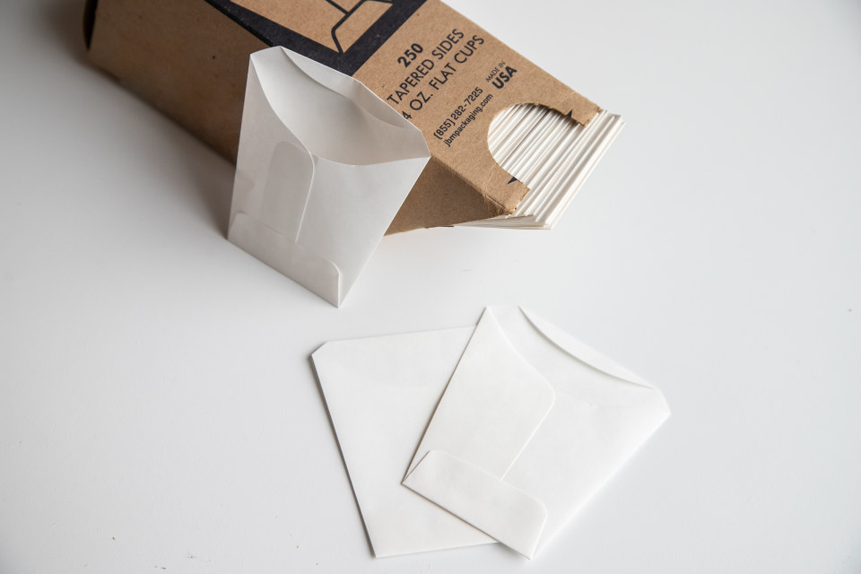 A cardboard box holds flat paper packages that can be used as small disposable cups.